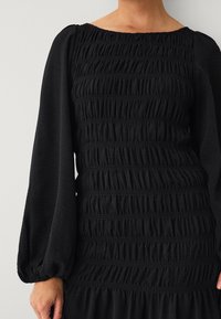 Schwarzes Kleid mit einem gerafften Design und horizontalen Rüschen, langen Puffärmeln und weitem Halsausschnitt. Glatte Textur, lässiger Stil.