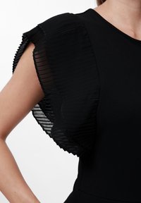 Abito nero con maniche trasparenti plissettate, dotato di un corpo in tessuto liscio e dettagli testurizzati sulle maniche. Design elegante e aderente.