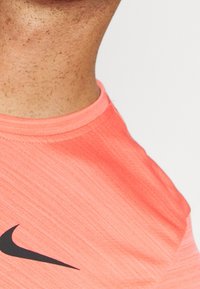 Camiseta deportiva de manga corta en color coral con una tela texturizada. Presenta un logo negro de Nike en el lado izquierdo y un diseño de cuello redondo.