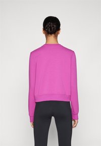 Sudadera fucsia con cuello redondo, mangas largas y corte relajado. Textura suave con puños y dobladillo de canalé, combinada con leggings negros.