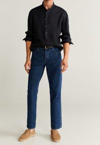 Camicia di lino nera con colletto alla francese e chiusura con bottoni. Indossata con jeans in denim blu e scarpe slip-on color cammello. Look semplice e casual.