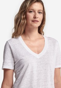 Vit, kortärmad T-shirt med V-ringning gjord av ett lätt och strukturerat tyg. Har en ribbad halsringning och en avslappnad passform.