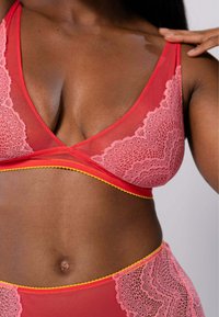 Rood lingerie set met doorzichtige stof, roze kantaccenten en gele afwerking langs de randen; zachte textuur met een driehoekig cupdesign.