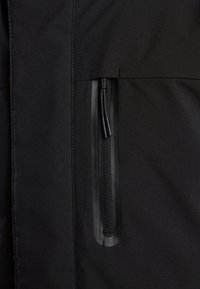 Musta takin kangas, jossa on sivuivetoketjupussi, sileä vetoketjun kahva, teksturoitu materiaali ja siistit saumat reunoilla.