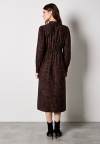 Abito lungo nero a maniche lunghe con stampa leopardata marrone, caratterizzato da una vita elasticizzata e una silhouette dritta, abbinato a stivaletti.