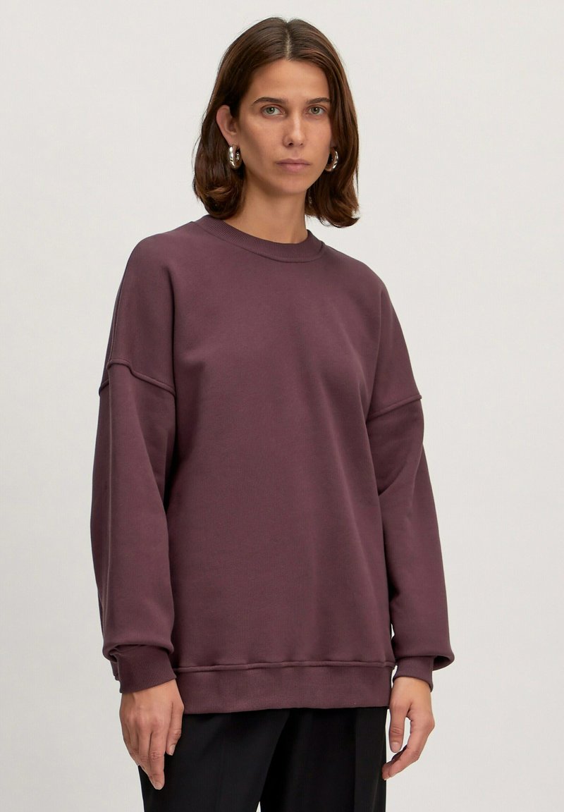 Bordeauxfarbenes Sweatshirt mit Rundhalsausschnitt, übergroßer Passform und abgesenkten Schultern. Hergestellt aus weichem Stoff mit gerippten Bündchen und Saum.