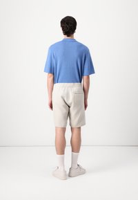 Camisa de punto de manga corta azul, pantalones cortos elásticos de cintura gris claro con bolsillo trasero, calcetines blancos, zapatos claros, vistos desde atrás.