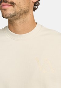 Felpa beige con un collo a girocollo testurizzato e un logo ricamato di colore simile sul petto. Tessuto morbido con una finitura liscia.
