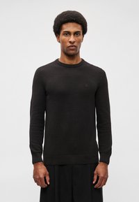Černý, texturovaný pletený svetr s dlouhými rukávy a kulatým výstřihem. Jemný logo detail na hrudi. Měkký materiál, přiléhavý střih.