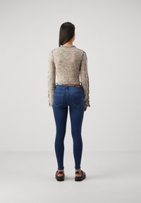 Top ligero de manga larga de punto multicolor con puños fruncidos, acompañado de jeans skinny azul oscuro y sandalias de plataforma marrones.