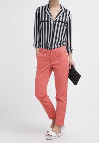 Pasiasta czarno-biała koszula na guziki, koralowe spodnie, białe sandały i czarna torebka. Swobodny krój o gładkiej fakturze i dopasowanym wzornictwie.