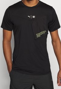 Svart atletisk t-shirt med texturerat tyg, har en framficka med neontext och Puma-logotyp. Kortsleeve, rund halsringning.