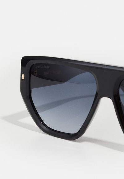 Occhiali da sole neri oversize con un design geometrico, lenti scure sfumate e un sottile dettaglio in oro sulla montatura.