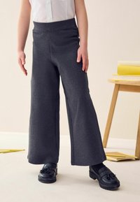 Pantalons gris évasés en tissu doux, dotés d'une taille haute et d'une texture subtile, associés à des chaussures noires à pampilles.