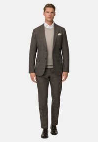 Completo grigio testurizzato slim fit, indossato sopra un maglione grigio chiaro. Camicia bianca sotto e un fazzoletto bianco nella giacca.