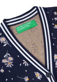 Mörkblå cardigan med vit randig krage, blommönster i ljuslila och gult, med en mörk knapp och etikett från United Colors of Benetton.