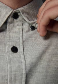 Cămașă din corduroy de culoare gri deschis, cu un design cu butoane, butoane negre și o textură ribbed pe țesătură. Prim-plan al detaliului color.