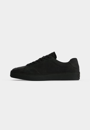 Baskets basses noires avec lacets à l'avant et semelle épaisse, vues de côté sur un fond uni clair.