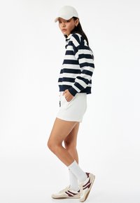 Marineblauw en wit gestreepte sweatshirt met hoge hals, gecombineerd met een witte korte rok. Compleet met witte sokken en beige-rode sneakers.