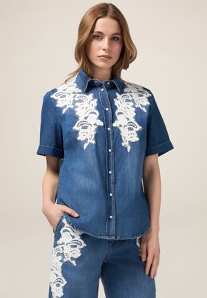 Camicia di jeans a maniche corte, con ricami floreali bianchi sulle spalle e bottoni sul davanti. Vestibilità tailored con tasca laterale.