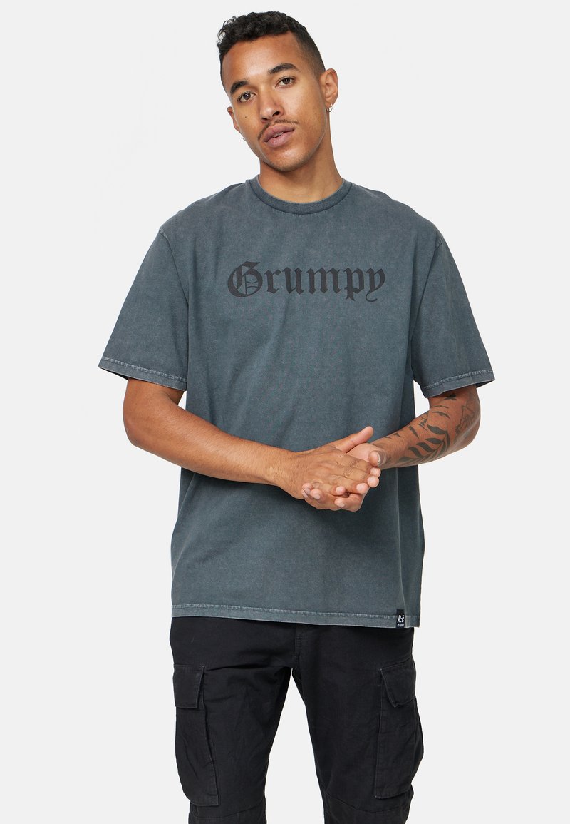 Camiseta de algodón gris con un estampado negro de "Grumpy" en una fuente audaz, de manga corta y ajuste holgado. Detalle de costura notable en el dobladillo.