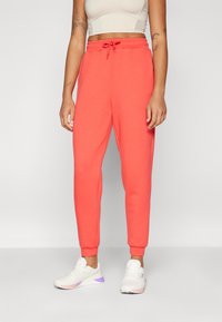 Korallfargede joggebukser med snor i midjen, smale ben og ribbede mansjetter. Kombinert med hvite sneakers med lilla detaljer.