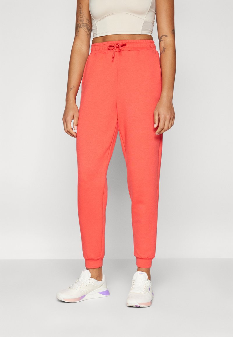 Korallfargede joggebukser med snor i midjen, smale ben og ribbede mansjetter. Kombinert med hvite sneakers med lilla detaljer.
