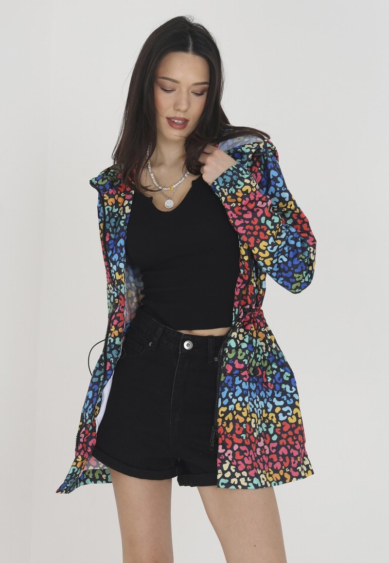 Veste légère et colorée avec un imprimé animal multicolore. Dotée d'une capuche et d'une taille à cordon. Associée à un haut noir et à un short.