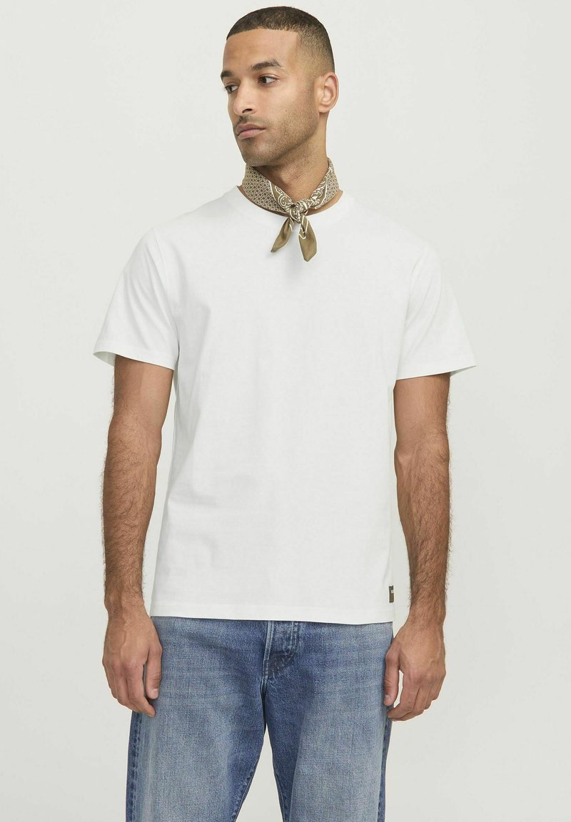 White cotton t-shirt with short sleeves, round neckline, and a subtle brand tag at the hem, paired with a patterned brown neck scarf.