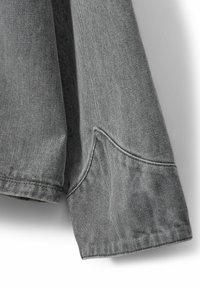 Manica di giacca in denim grigio con cuciture visibili, dettaglio della tasca e una texture leggermente sbiadita, con un design pulito e casual.