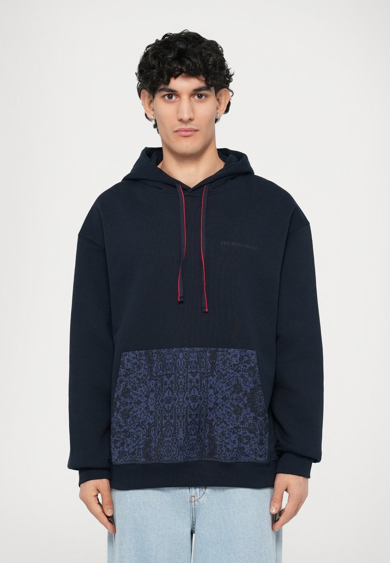 Marinefarbener Kapuzenpullover mit einer Kängurutasche, die ein dunkles Musterdesign aufweist. Dekorative rote Zugbänder, lässiger Schnitt, aus Baumwollmaterial.