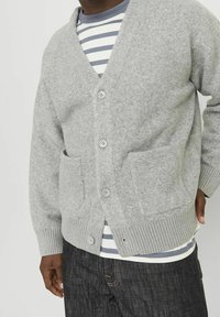 Grå stickad cardigan med V-ringning, fem knappar, två framfickor, ribbade ärmslut och nederkant, bärs över en randig T-shirt.