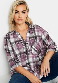 Camicia a scacchi viola e bianca con vestibilità ampia, maniche arrotolabili e taschino sul petto con bottone. Tessuto morbido con una leggera trama.