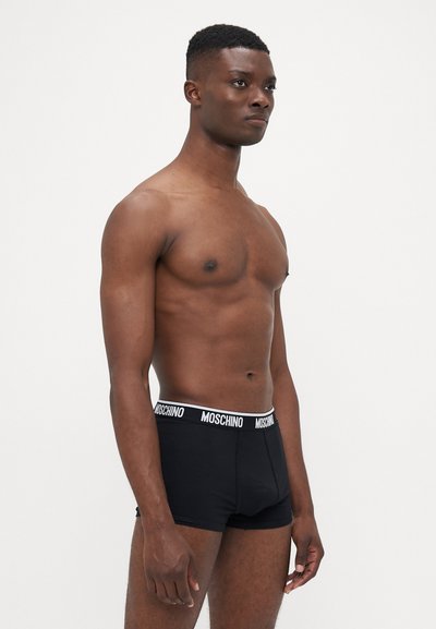 Black boxers featuring a white Moschino logo waistband; smooth fabric, fitted design, mid-thigh length, minimal seams.