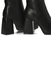 Botas de tobillo de cuero negro con tacones cuadrados, que cuentan con una cremallera lateral y una textura suave. Los tacones son de forma cuadrada y resistentes.