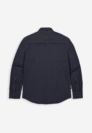 Schwarzes, langärmliges Hemd mit Knöpfen, flach liegend und von hinten gezeigt, mit Manschetten und einem geraden Einsatz über den Schultern.