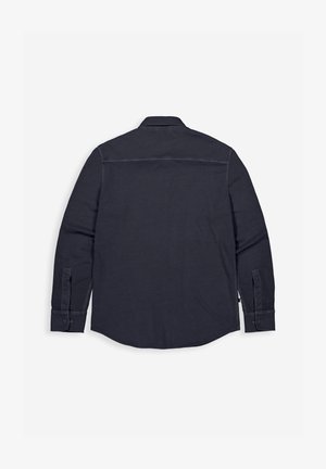 Schwarzes, langärmliges Hemd mit Knöpfen, flach liegend und von hinten gezeigt, mit Manschetten und einem geraden Einsatz über den Schultern.