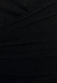 Svart stickat tyg med en texturerad yta, med lager eller draperade sektioner som skapar visuell intresse och djup.