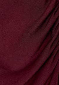 Burgundi színű anyag sima textúrával, puha eséssel és finom redőzéssel, amelyek visszafogott mélységet és mozgást kölcsönöznek az anyagnak.