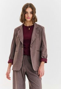 Brązowy dwurzędowy blezer w kratę z pojedynczym zapięciem na guzik, klapami z wycięciem i podwiniętymi bordowymi rękawami, zestawiony z bordowym topem.