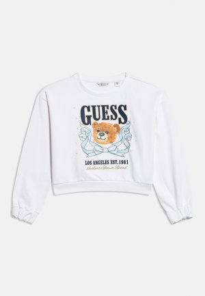 White long-sleeve cropped sweatshirt with a teddy bear, large "GUESS" text, blue ribbon, and "LOS ANGELES EST. 1981" printed below.