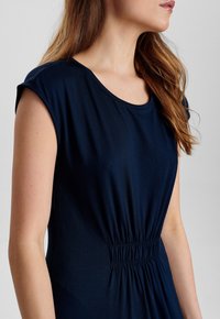 Abito blu navy con scollo rotondo, maniche corte e vita elasticizzata. Tessuto morbido con una texture liscia e dettagli arricciati.