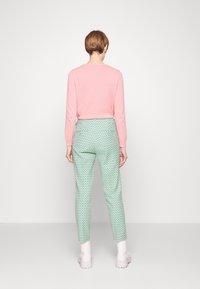 Suéter de punto en color rosa claro y pantalones verdes menta con un patrón estampado. Los pantalones tienen un diseño ajustado con un pequeño patrón geométrico repetido.