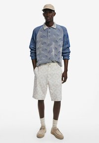 Polo cu maneci lungi, albastru și alb cu un model, pantaloni scurți crem cu un design subtil, încălțăminte bej și o pălărie bej. Texturi moi, croială casual.