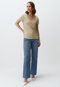 Beżowa koszulka z dekoltem w serek zestawiona z jasnoniebieskimi spodniami o szerokich nogawkach i białymi szpilkami o ostrych noskach. Gładki materiał, luźny krój i widoczne detale szycia.