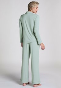 Lichtgroene pyjama-set van zacht materiaal, met een langemouwige knoopsluiting top en relaxte broek met wijde pijpen en manchetten.