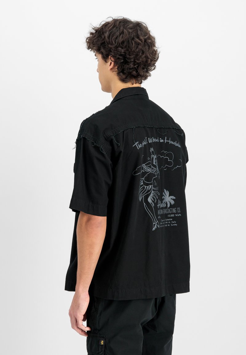 Zwarte t-shirt met korte mouwen met een grafisch ontwerp op de achterkant. Het ontwerp bevat een dansende figuur, een palmboom en tekst in lichtgrijs.