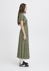 Green floral print maxi dress with short ruffled sleeves, fitted bodice, and flowing skirt; worn with black sneakers and white socks.