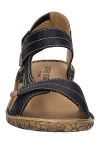 Mustan nahkasaapas, jossa on kaksi säädettävää remmiä, pehmustettu pohja ja teksturoitu kumipohja. Minimalistinen muotoilu ruskeilla yksityiskohdilla.