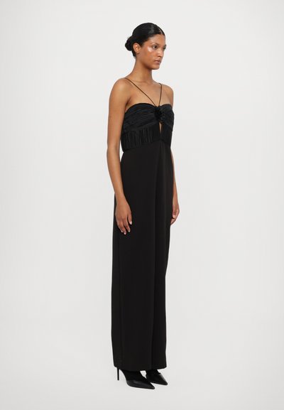 Zwarte jurk met een geplooide, strapless top en rechte benen. Heeft een centrale uitsnijding en delicate schouderbandjes. Draagt met puntige hakken.